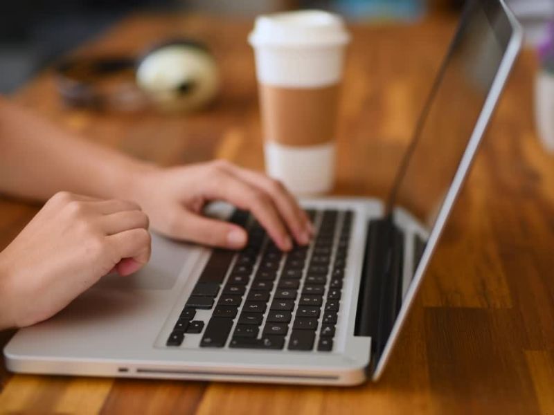 Devojka koristi laptop, pored nje plastična čaša za kafu