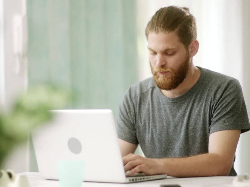 Momak u sivoj majici sedi i koristi laptop