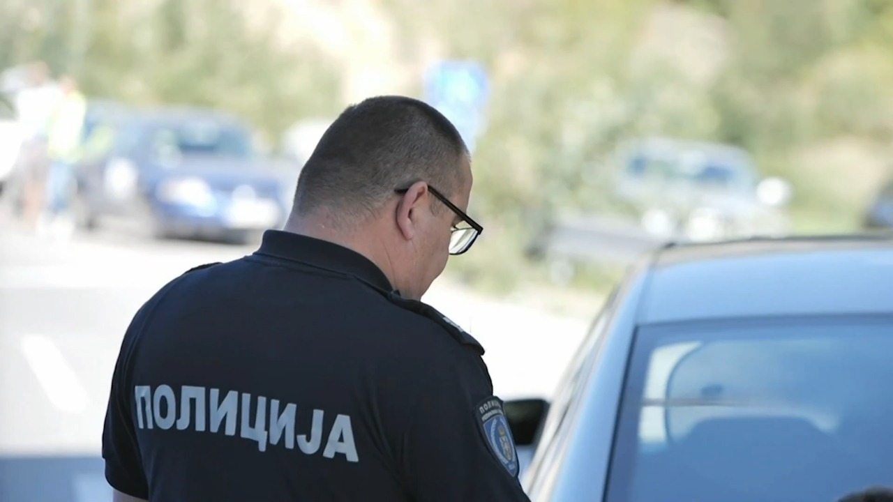 Policajac u uniformi stoji pored automobila i vrši kontrolu dok razgovara sa vozačem