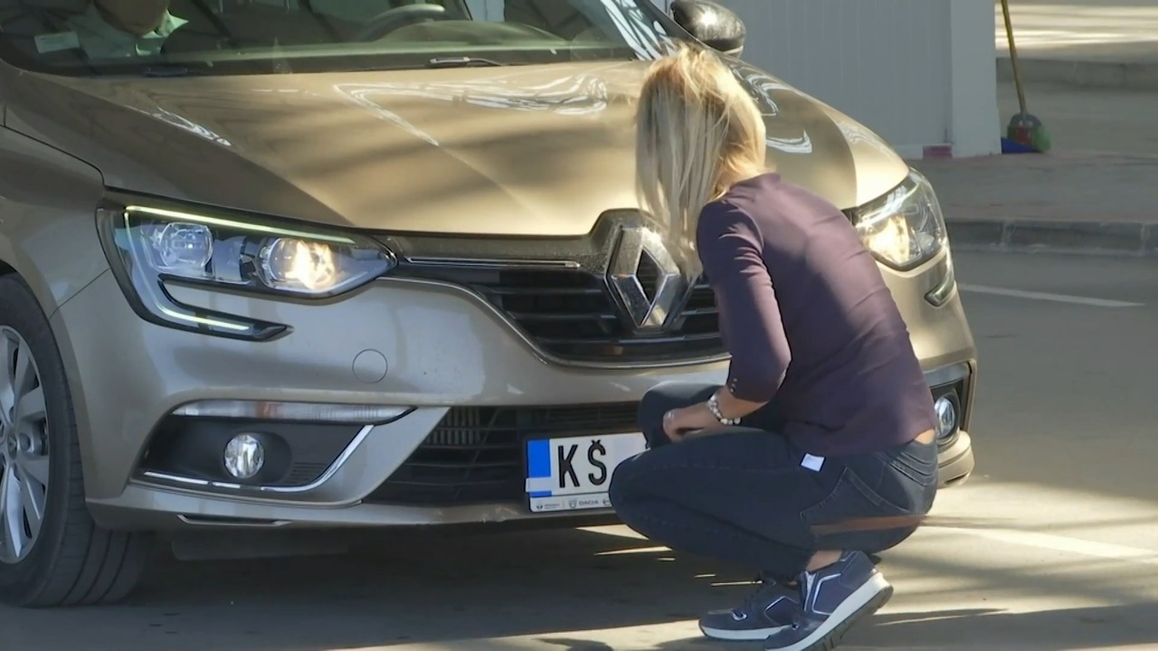 Žena čuči ispred automobila i proverava ili skida registarske tablice sa prednjeg branika