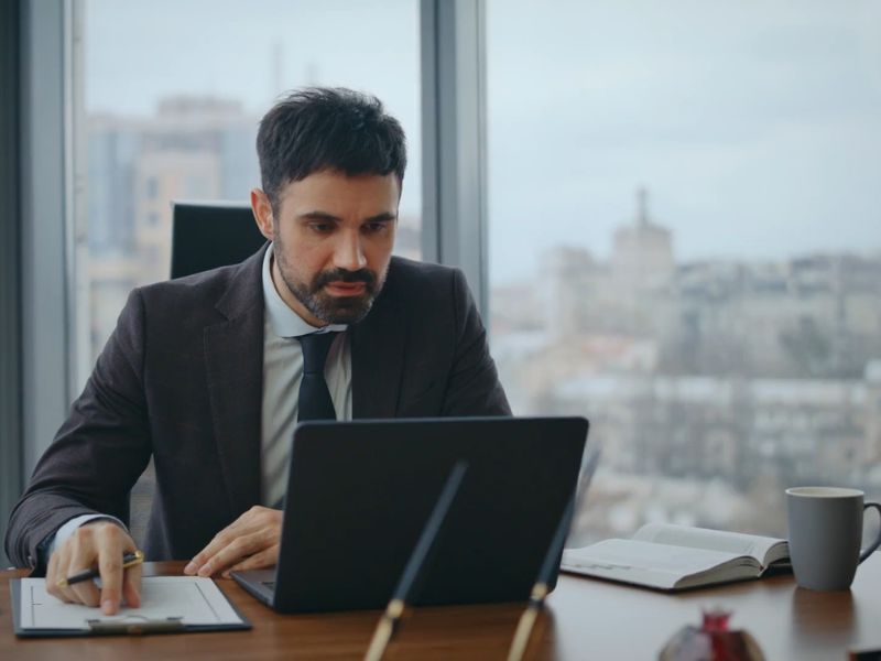 čovek radi u kancelariji za radnim stolom na kom je laptop