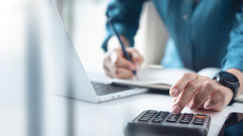 Knjigovođa za radnim stolom koristi kalkulator i laptop