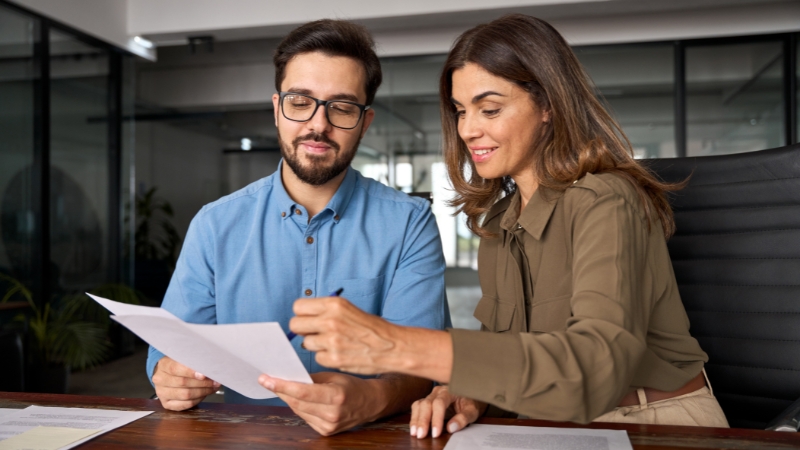 Muškarac i žena za stolom zajedno pregledaju dokument i razgovaraju o poslovnim podacima