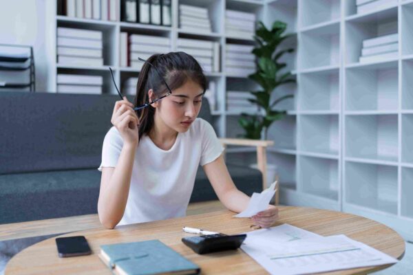 Žena proverava račun i dokumenta za stolom sa kalkulatorom