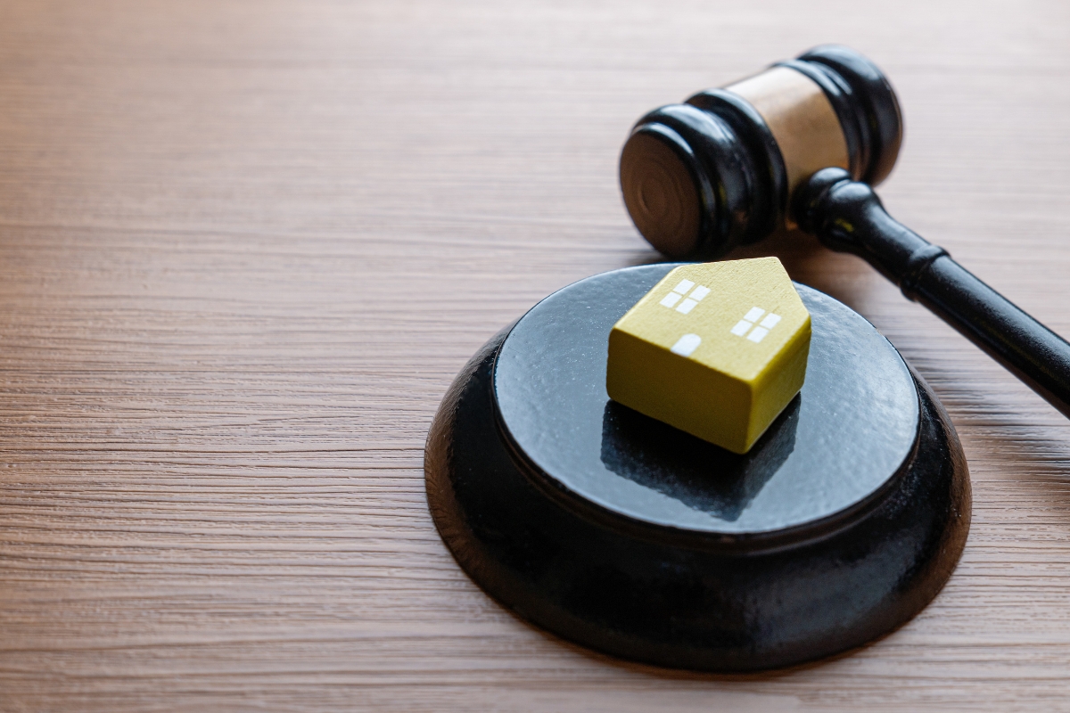 prikaz advokatske palice i kuće na drvenom stolu, simulirajući na advokatsku pomoć oko promene vlasnika i info stana
