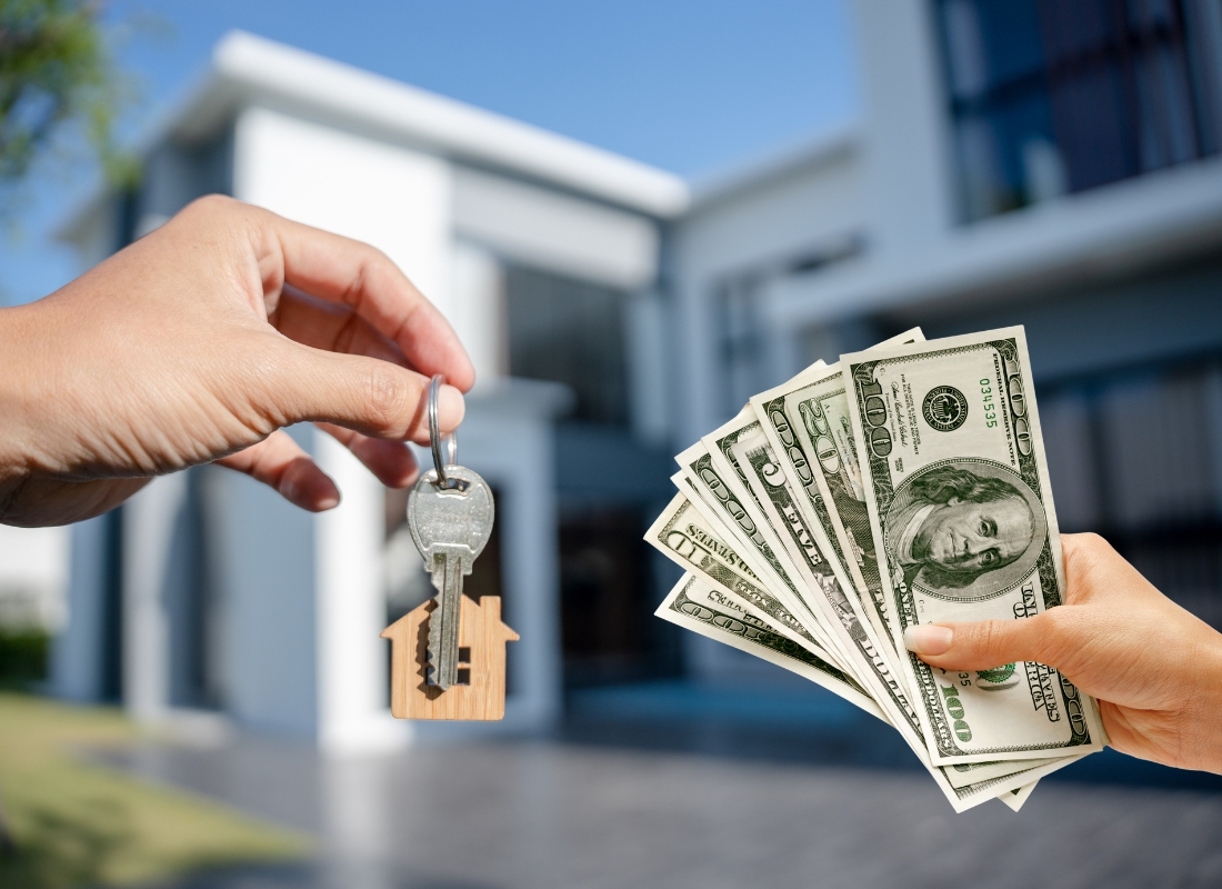 prikaz ključa, zgrade u pozadini i novca u ruci