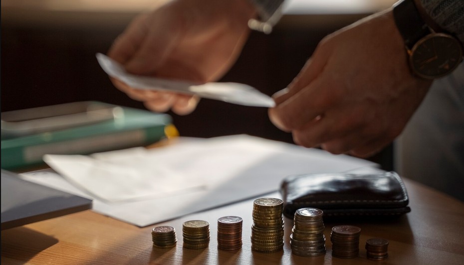 Osoba pregledava finansijska dokumenta za stolom na kojem se nalaze naslagani novčići različitih visina i novčanik